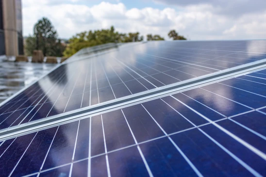 Ingénieur en casque blanc inspectant une installation photovoltaïque extérieure au coucher du soleil, tenant une tablette numérique, main en visière pour observer les panneaux