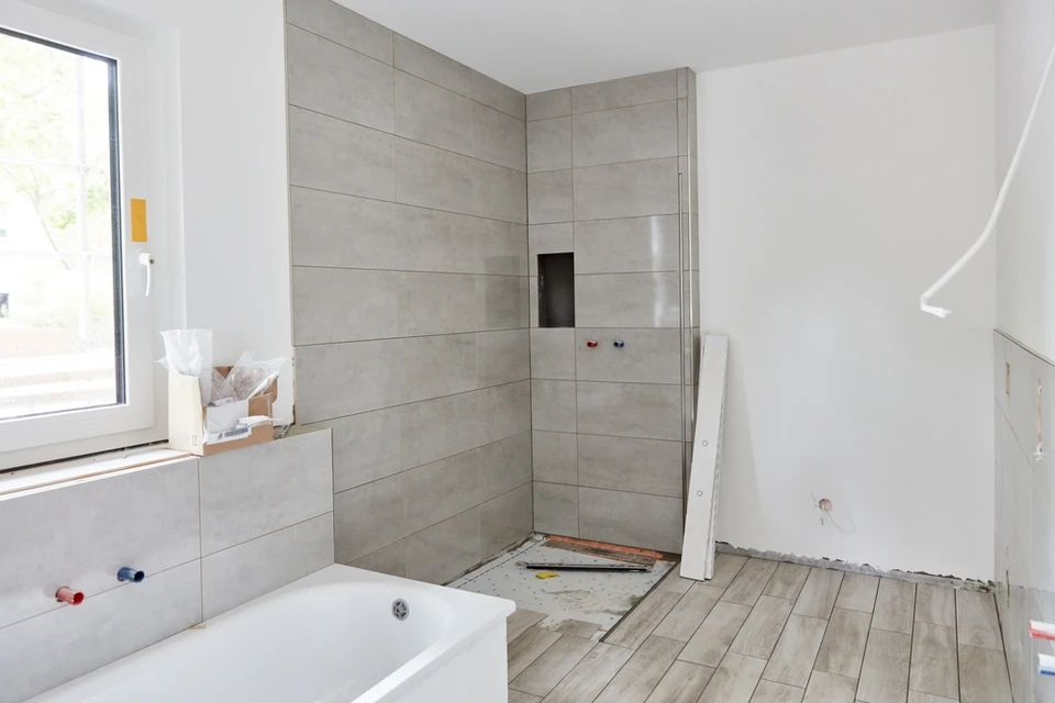Salle de bains en cours de rénovation avec baignoire blanche installée, murs carrelés gris partiellement posés